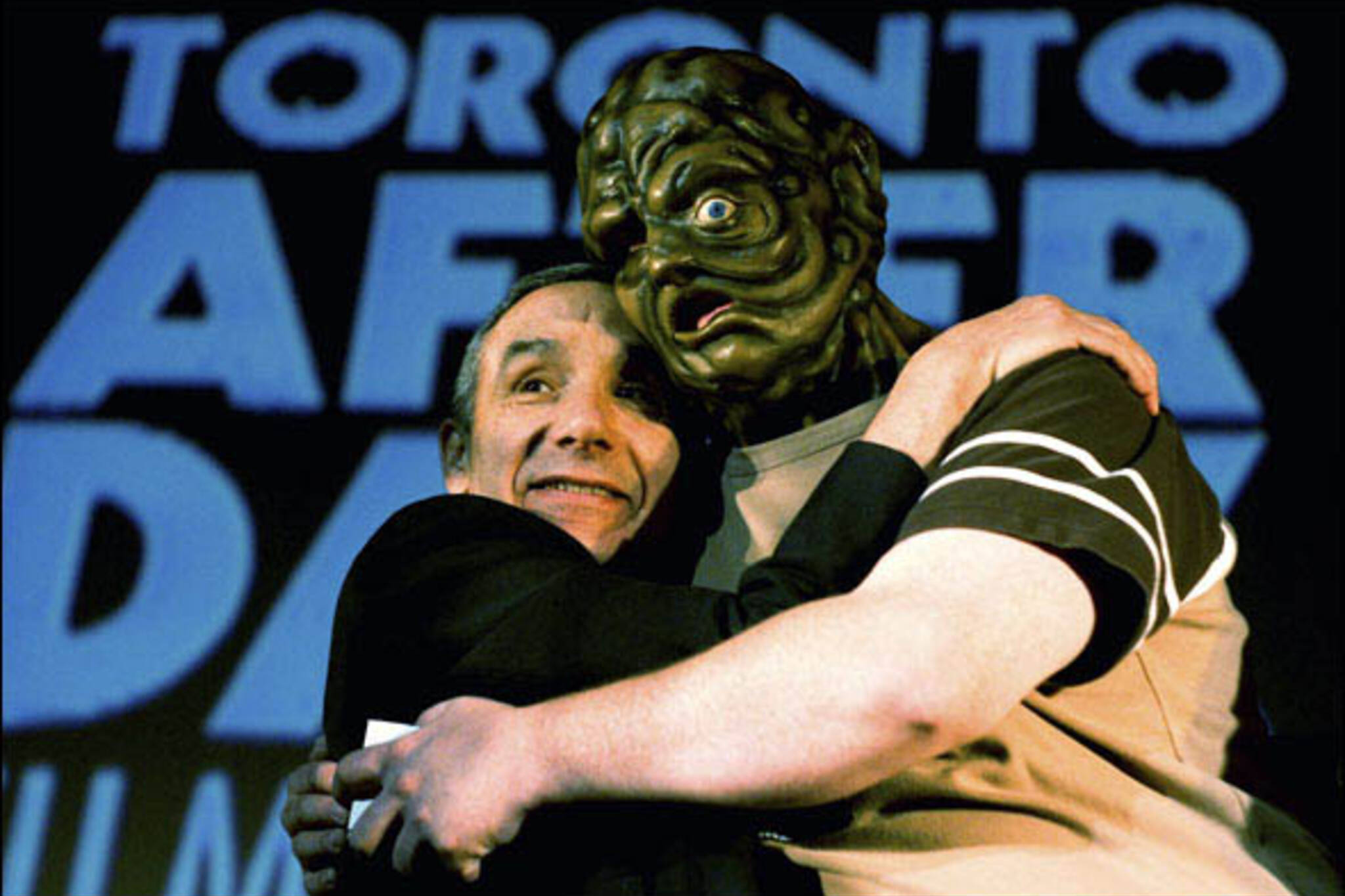 Director Lloyd Kaufman embraces a ghoulish creature on stage after the Toronto premiere screening of Poultrygeist: Night of the Chicken Dead at The Bloor Cinema during the Toronto After Dark Film Festival.